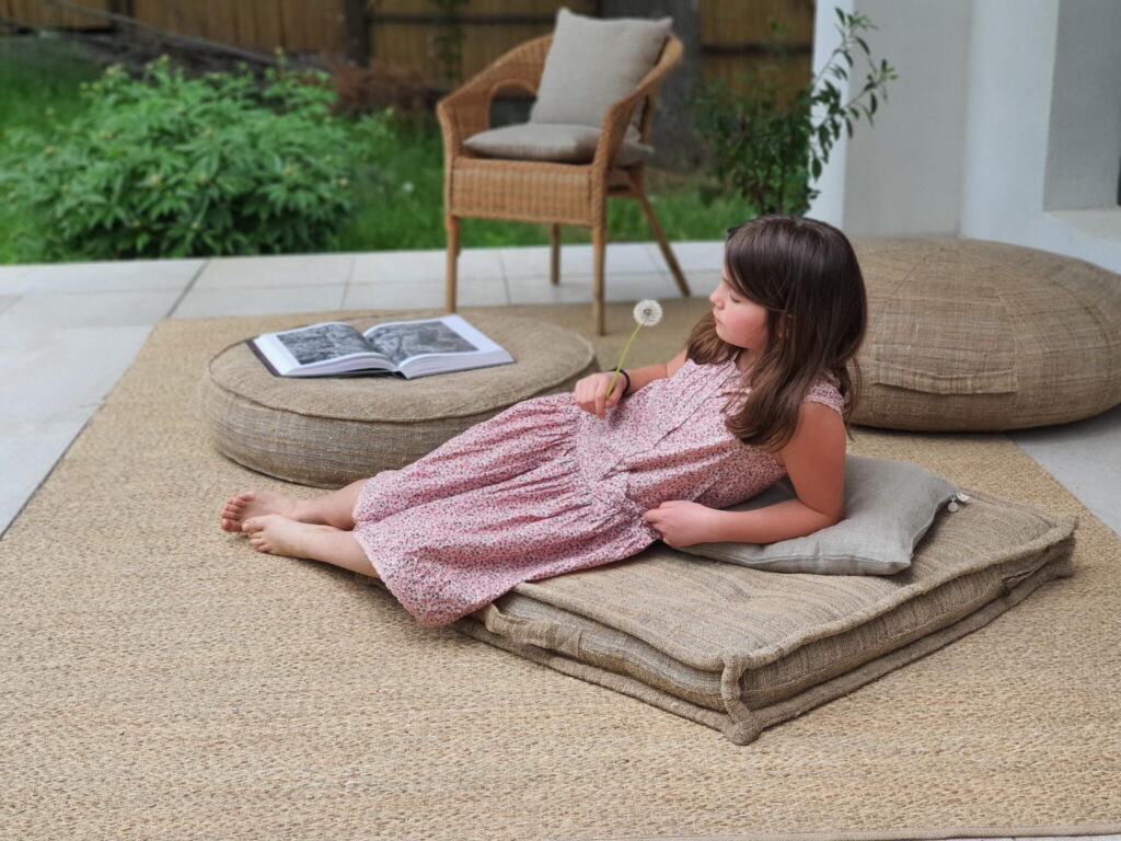 girl relaxing on wool cushions, holding a dandelion, beside open book
